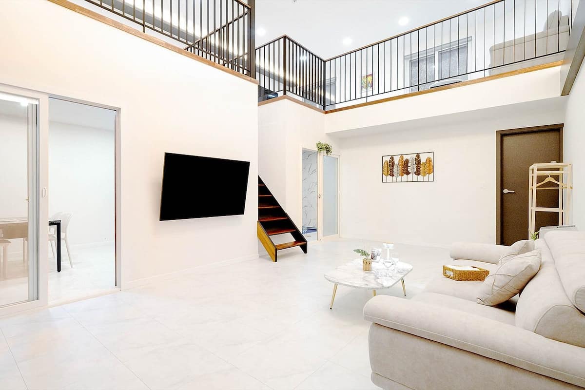 Un vaste espace de vie comprenant un canapé blanc, une table basse et un escalier menant à un balcon.
