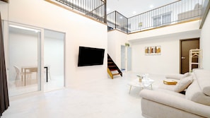 Un vaste espace de vie comprenant un canapé blanc, une table basse et un escalier menant à un balcon.