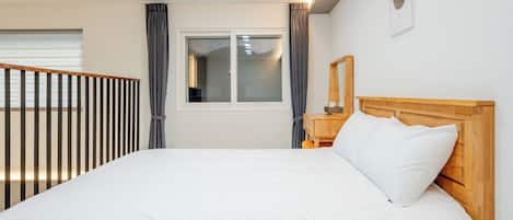 A hotel room with a large bed, a wooden headboard, a nightstand, a mirror, and a window with curtains.