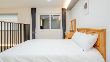 Et hotelværelse med en stor seng, et træhovedgærde, et natbord, et spejl og et vindue med gardiner.