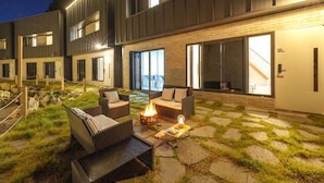 An outdoor patio area with seating, a fire pit, and a view of a modern building.