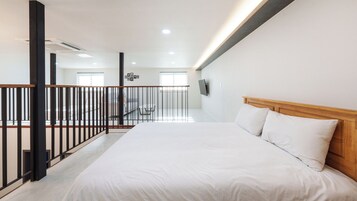Habitación de hotel con una cama, cabecera de madera, balcón con barandilla y un televisor montado en la pared.