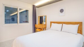 Une chambre d’hôtel avec un lit, une table de chevet en bois, un miroir et une fenêtre avec des rideaux.