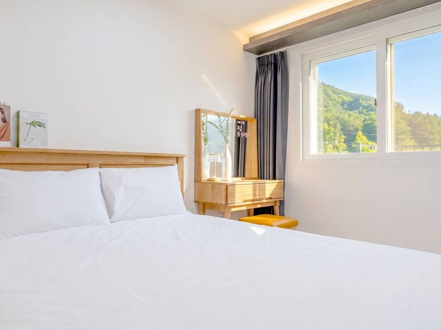 Een hotelkamer met een bed, nachtkastje, spiegel en raam met uitzicht op een bos.