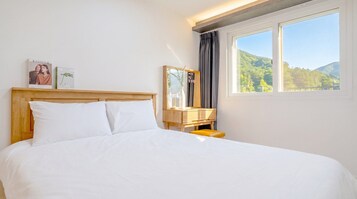 Habitación de hotel con una cama, una mesita de noche, un espejo y una ventana con vistas a un bosque.