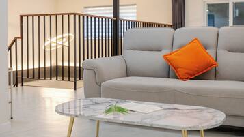A modern living room with a grey sofa, a marble coffee table, and a black railing staircase.