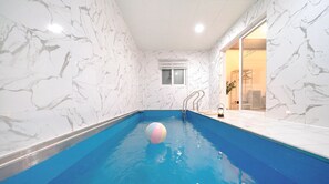 Une piscine intérieure aux murs de marbre, avec de l’eau bleue et un seul ballon.