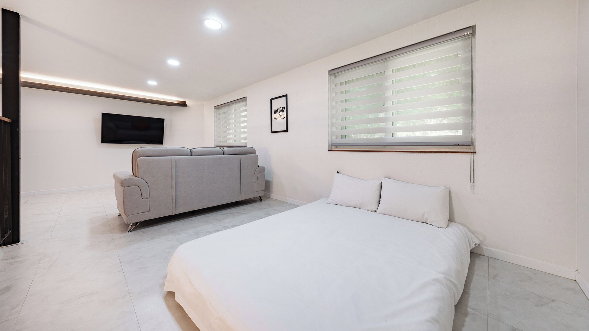 Un dormitorio moderno con una cama, un sofá, un televisor y un ventanal con persianas.