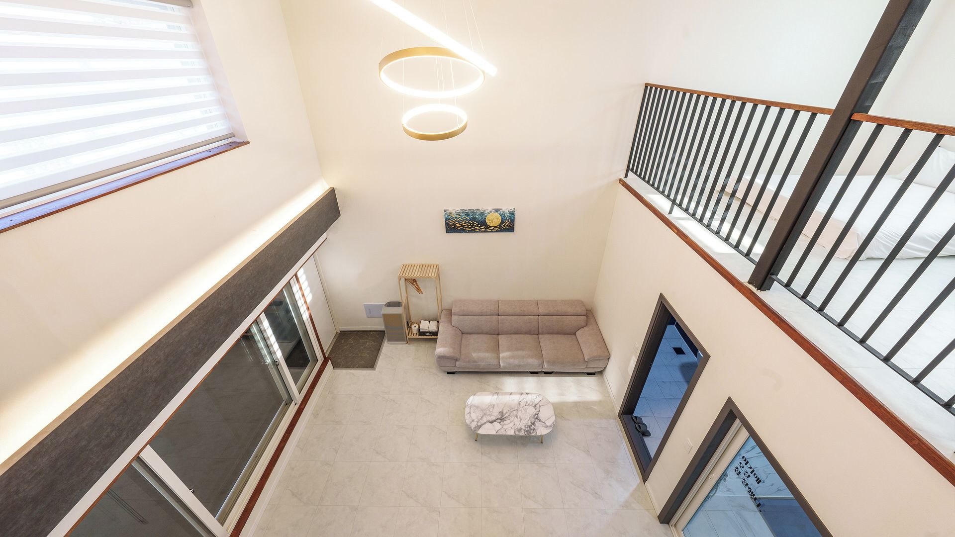 Een meerlaags interieur met een bank en een klein tafeltje, een schilderij aan de muur en een trap met een leuning.