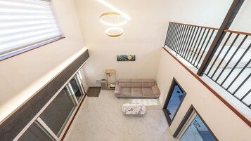 A multi-level interior with a sofa and a small table, a painting on the wall, and a staircase with a railing.
