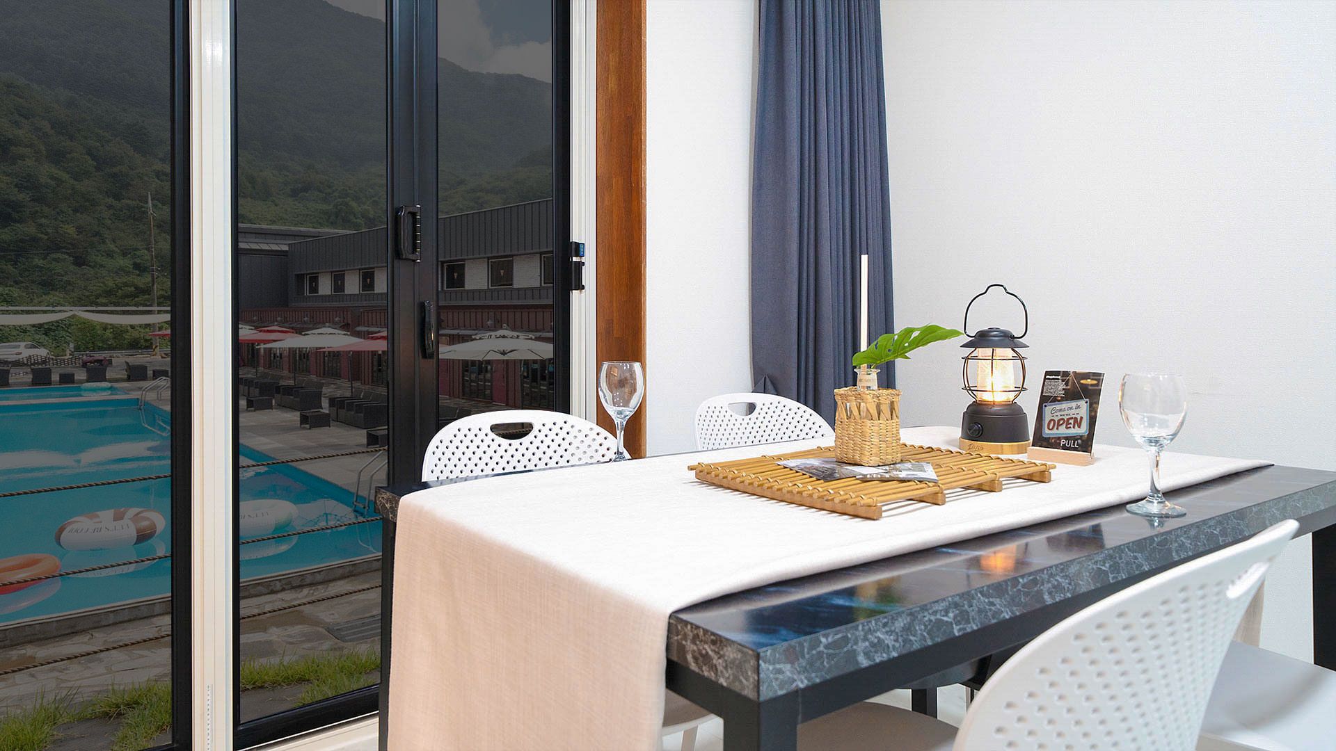 A dining area with a table set for two, a view of a pool, and a mountain landscape.