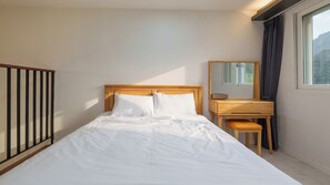 Un dormitorio con cama, un escritorio de madera, una silla, un espejo y una ventana con cortinas.