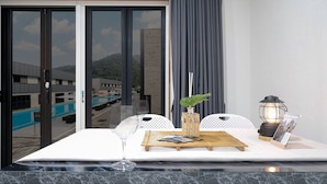 A dining area with a table set for two, a view of a swimming pool, and a cityscape in the background.