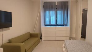Ein Zimmer mit einer Couch, einem Bett, einem Fenster mit Vorhängen und einem Fernseher.