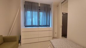 Ein Schlafzimmer mit Bett, einem Fenster mit Vorhängen, einem Kleiderschrank und einer Tür.