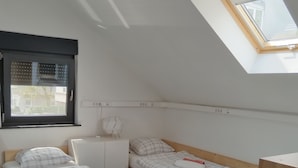 Ein Schlafzimmer mit zwei Holzbett, einem Oberlicht, einem Fenster und einem weißen Kleiderschrank.