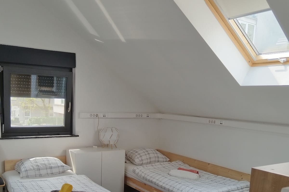 A bedroom with two wooden beds, a skylight, a window, and a white wardrobe.