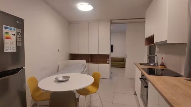 Eine kleine Küche mit Kühlschrank, Spüle und einer Holz Arbeitsplatte. Ein kleiner Esstisch mit zwei Stühlen steht bereit.