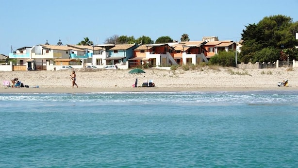 A beach with houses in the background and a person swimming in the water. - Apartment B6 third row first floor (Fondo Morte)