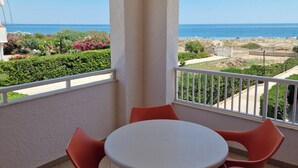 A covered outdoor area with a round table and four chairs, overlooking a beach with a clear view of the sea and distant landscape. - Apartment B6 third row first floor (Fondo Morte)