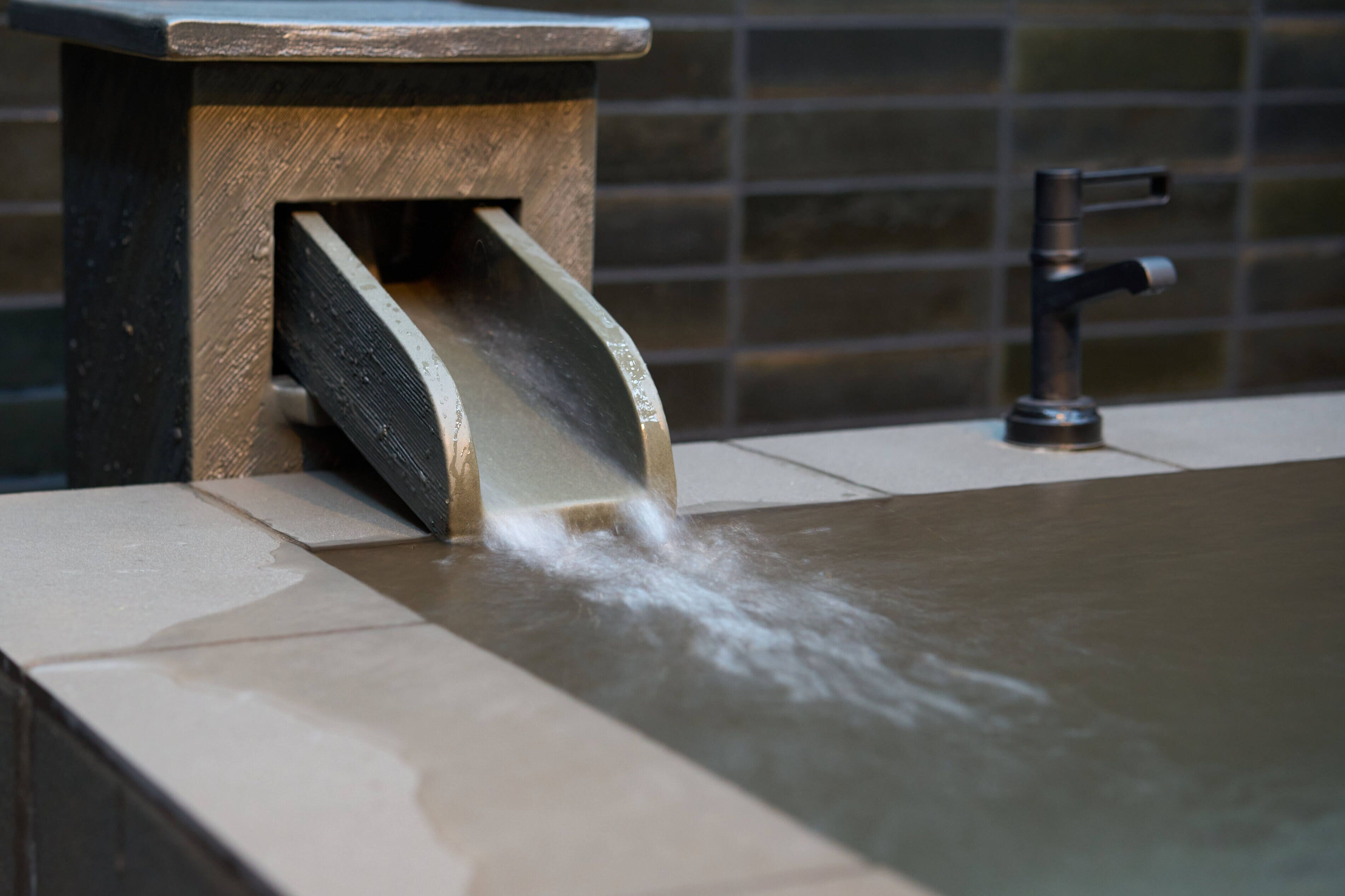 A spa area with a water feature, a stone ledge, and a tiled wall.