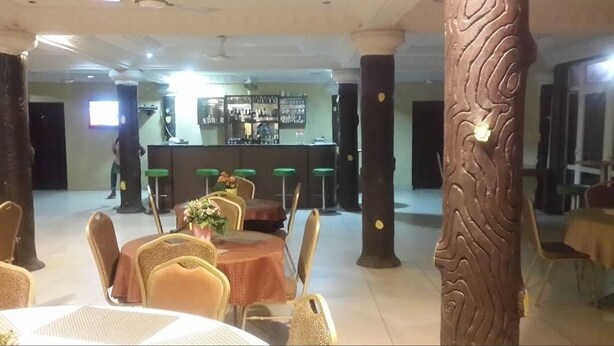 Un restaurant avec des tables et des chaises rondes, un bar situé au fond de la salle et des piliers ornés de motifs décoratifs.