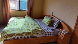 Un lit simple avec une couvre-lit à motifs et des oreillers, un téléphone sur la table de chevet et une fenêtre avec des rideaux.