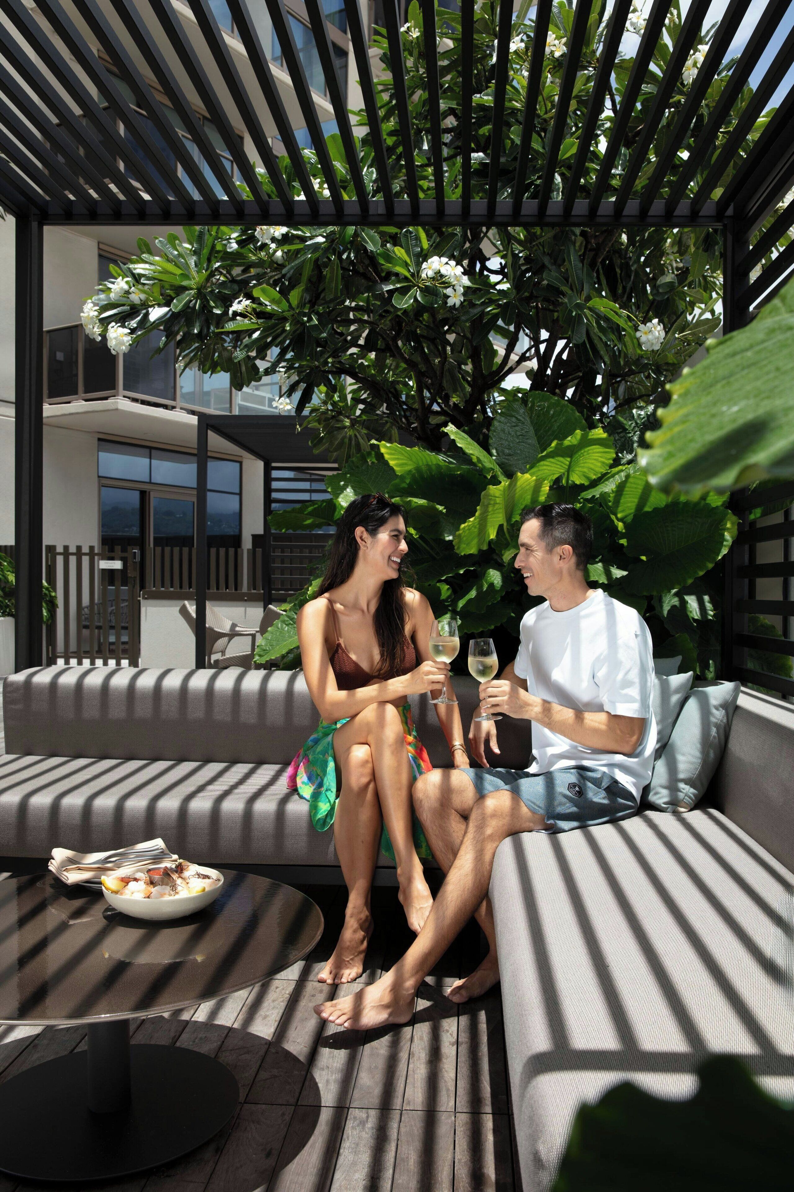 A modern outdoor seating area with a cushioned sofa, a round table with a bowl of food, and a pergola overhead.