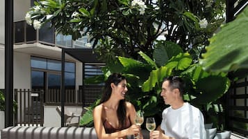 A modern outdoor seating area with a cushioned sofa, a round table with a bowl of food, and a pergola overhead.