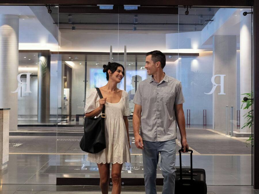 Een moderne hotel lobby met een glazen entree, een houten plafond en een zichtbare trap op de achtergrond.