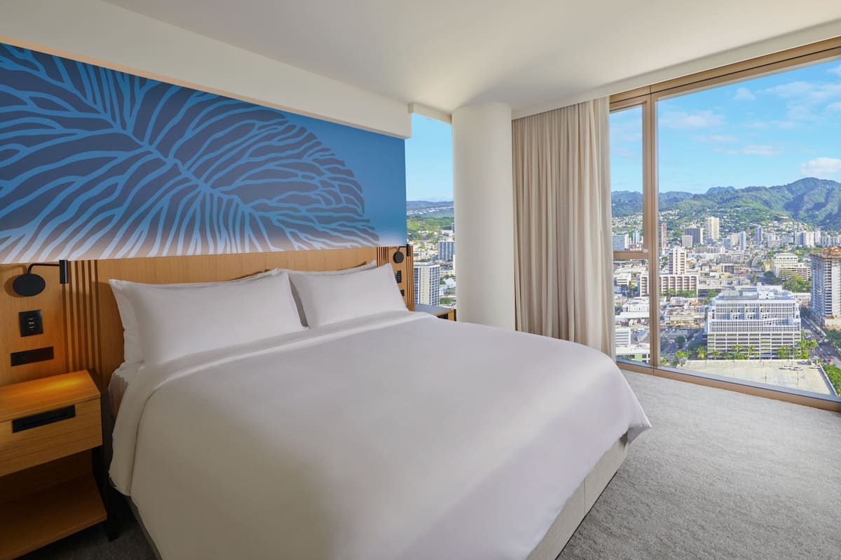 A hotel room with a large bed, a city view, and a blue leaf design on the wall.