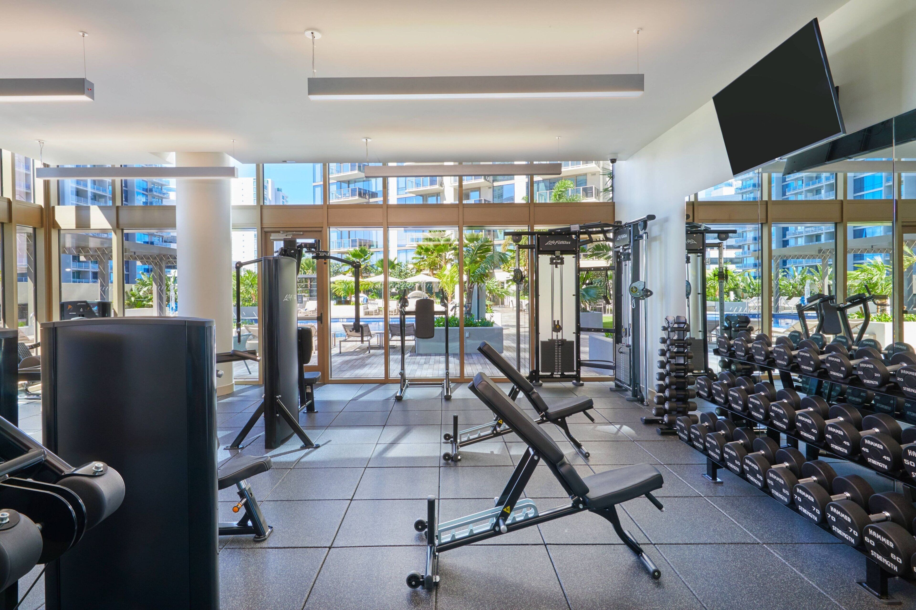 Et fitnesscenter med forskellig træningsudstyr, store vinduer og udsigt udad.