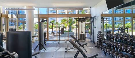 A gym with various exercise equipment, large windows, and a view of the outside.