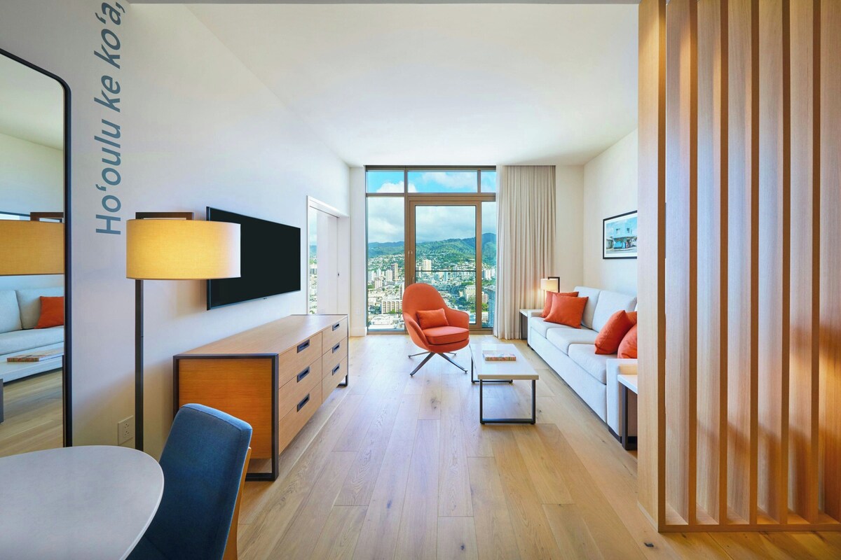 Una habitación de hotel moderna con vista a la ciudad, un televisor de pantalla plana, un sofá, una mesa de comedor y una silla.