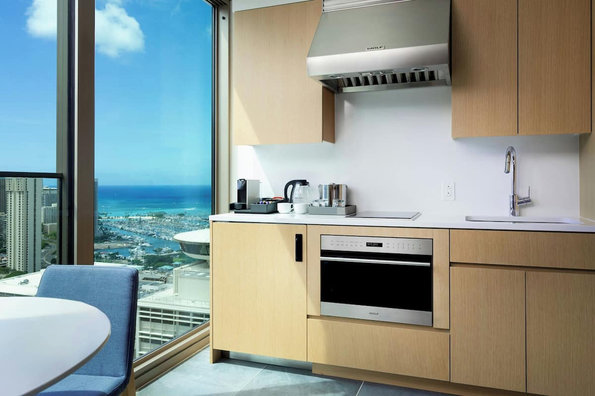A modern kitchen with a built-in oven and dishwasher, a coffee maker, and a view of the city and ocean.