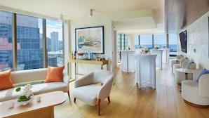 Una sala de estar moderna con sofá, sillón y mesa de centro, una zona de bar y ventanas amplias con vista a la ciudad.