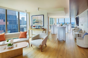 A bar area with wooden bar stools, a counter with shelves of bottles, and blue cushioned seating. at Renaissance Honolulu Hotel & Spa