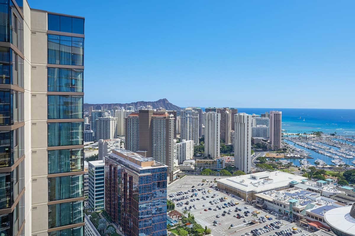 A high-rise building with a parking lot in front, a marina with boats, and a clear blue sky.