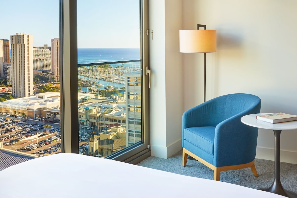 A hotel room with a large window offering a view of a cityscape and the ocean.