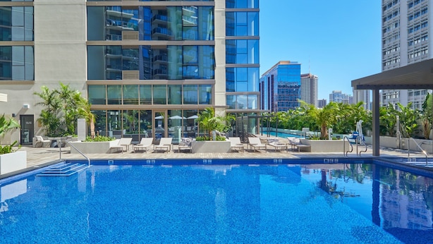 Un hotel moderno con piscina en la azotea, sillones de descanso y vistas de edificios altos circundantes.