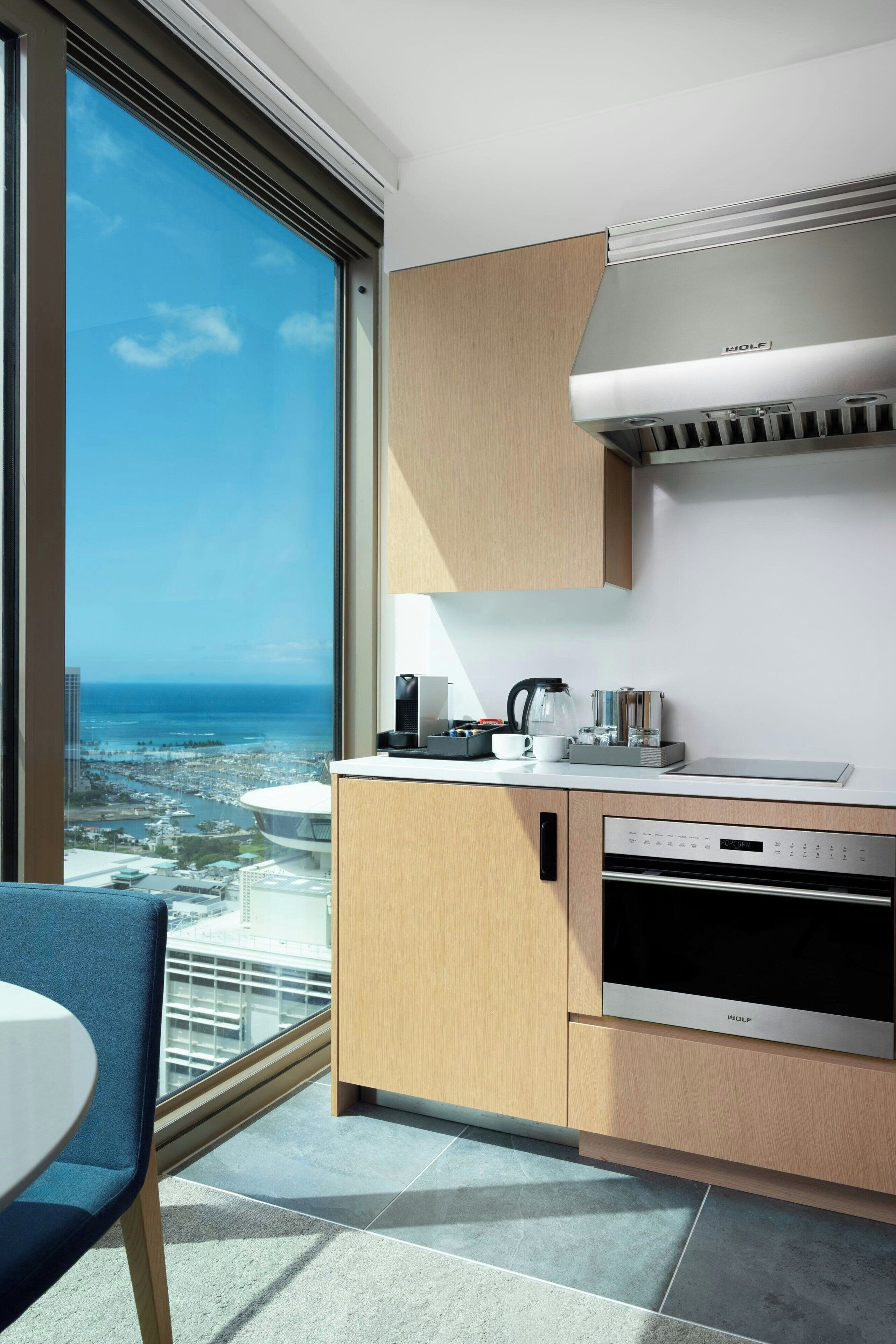 A modern kitchen with a view of the city and ocean, a coffee maker, and a dishwasher.