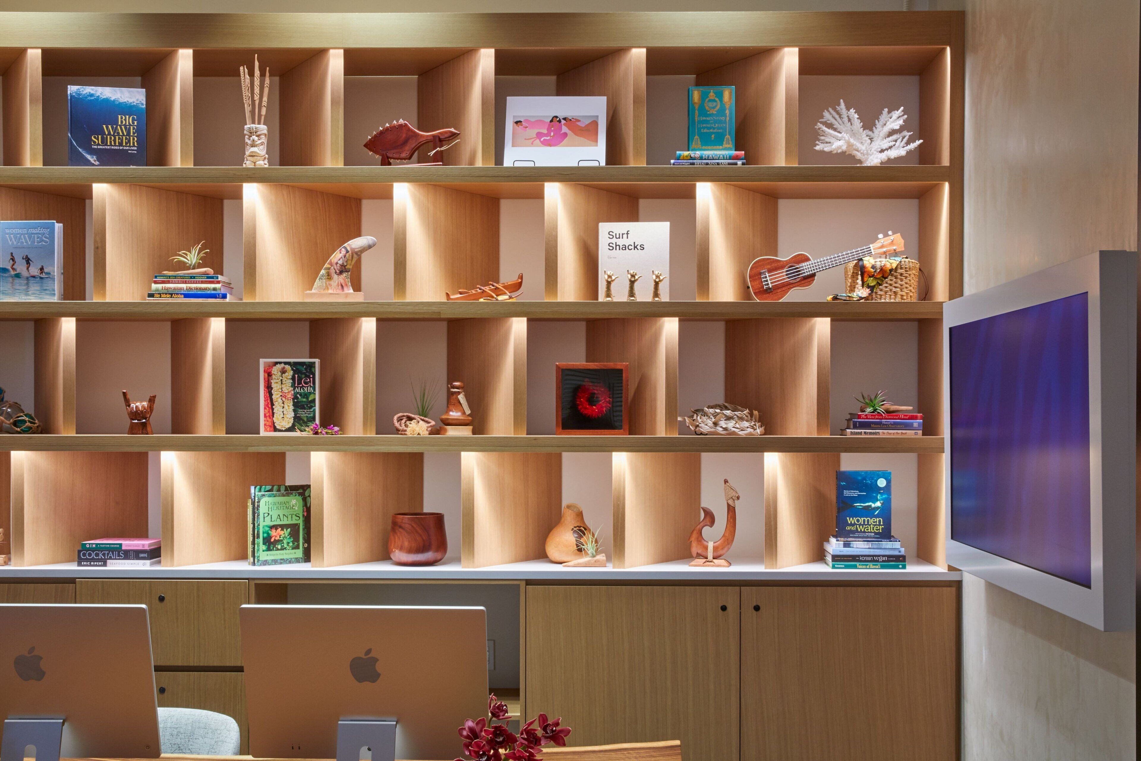 A modern library with wooden shelves containing books, decorative items, and a sign about surf shacks.