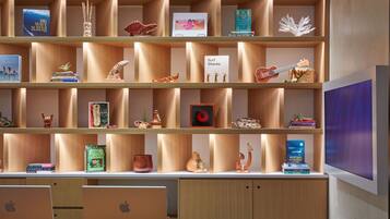 A modern library with wooden shelves containing books, decorative items, and a sign about surf shacks.