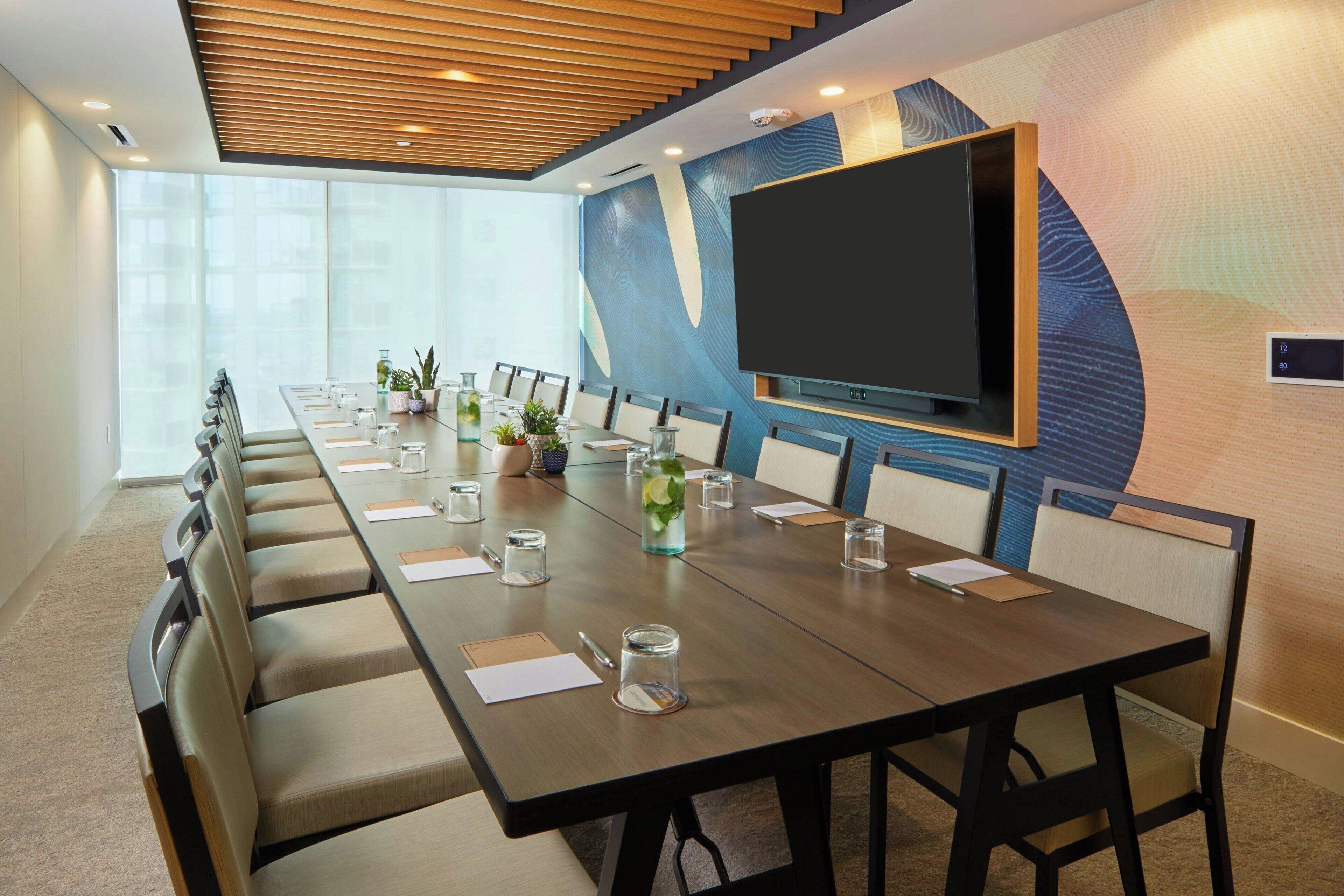 Un salón de conferencias con una larga mesa, sillas, un televisor y una decoración de pared.