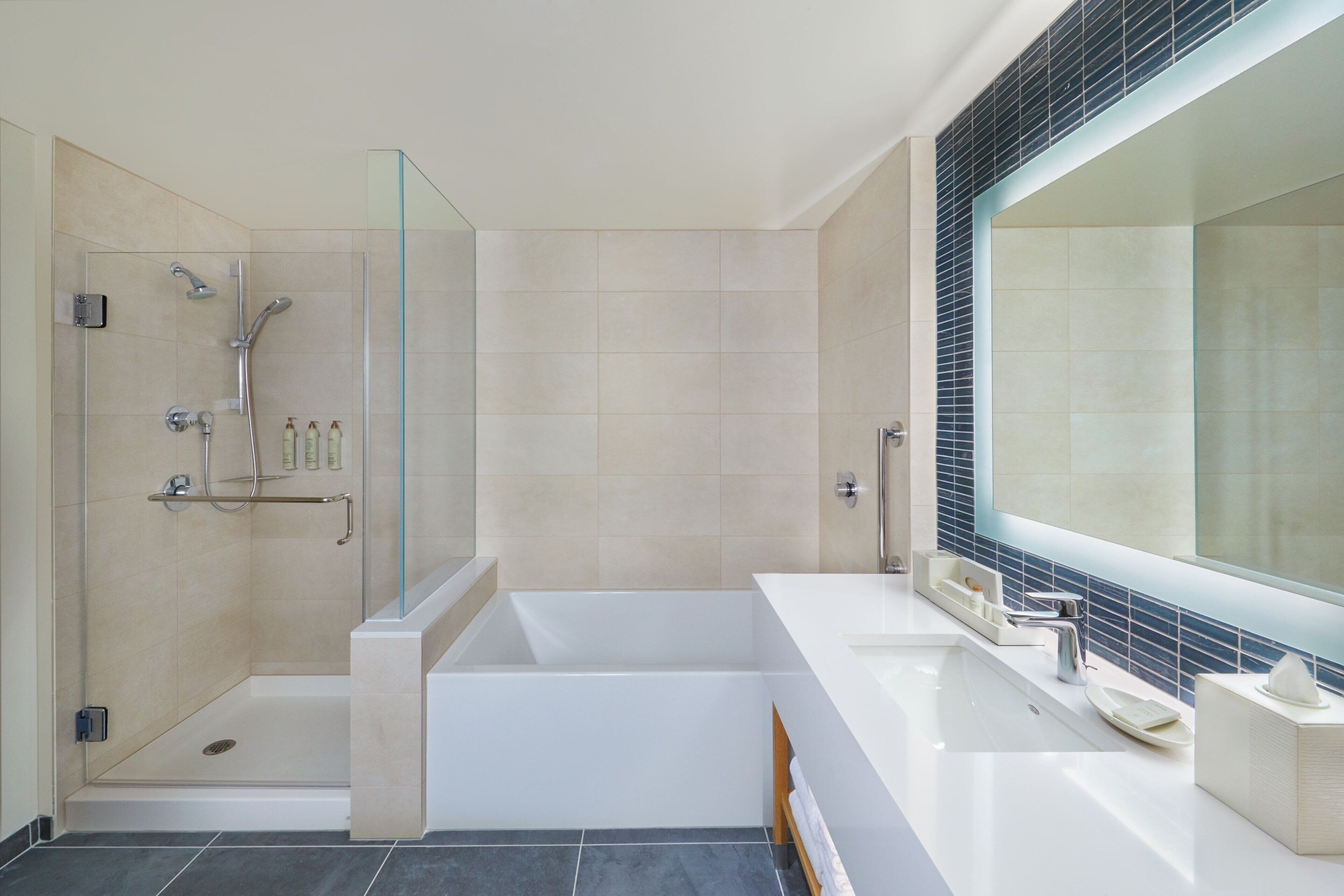 Een moderne badkamer met een douchecabine van glas, een vrijstaand bad en een grote spiegel boven de wastafel.