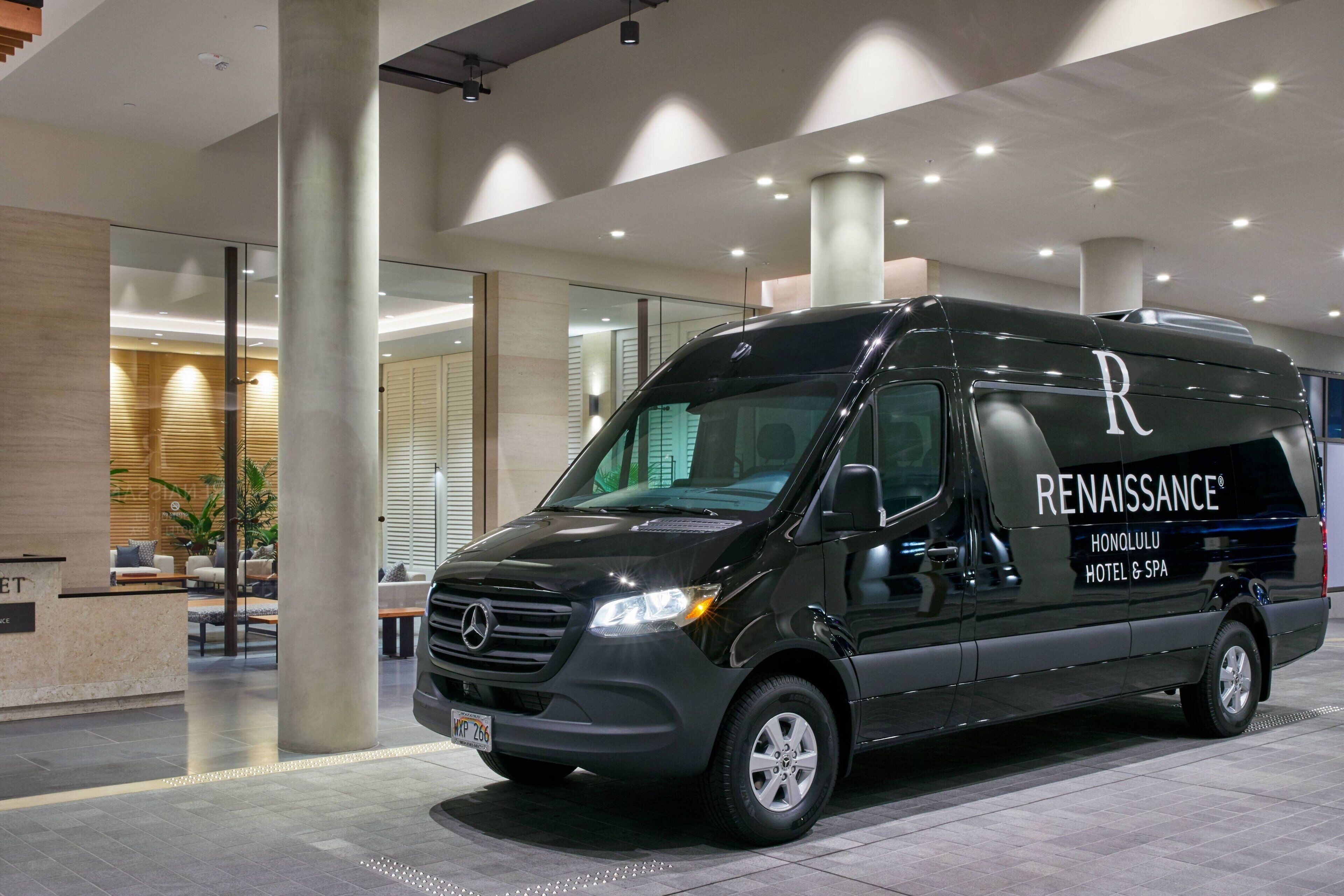 Ein schwarzer Mercedes-Benz RENAISSANCE Transporter steht in der modernen Lobby eines Hotels mit Empfangsbereich und Sitzgelegenheiten.
