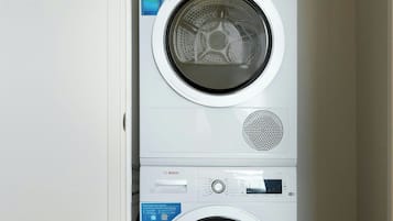 A stacked washer and dryer unit in a laundry room with a door and a metal handle.