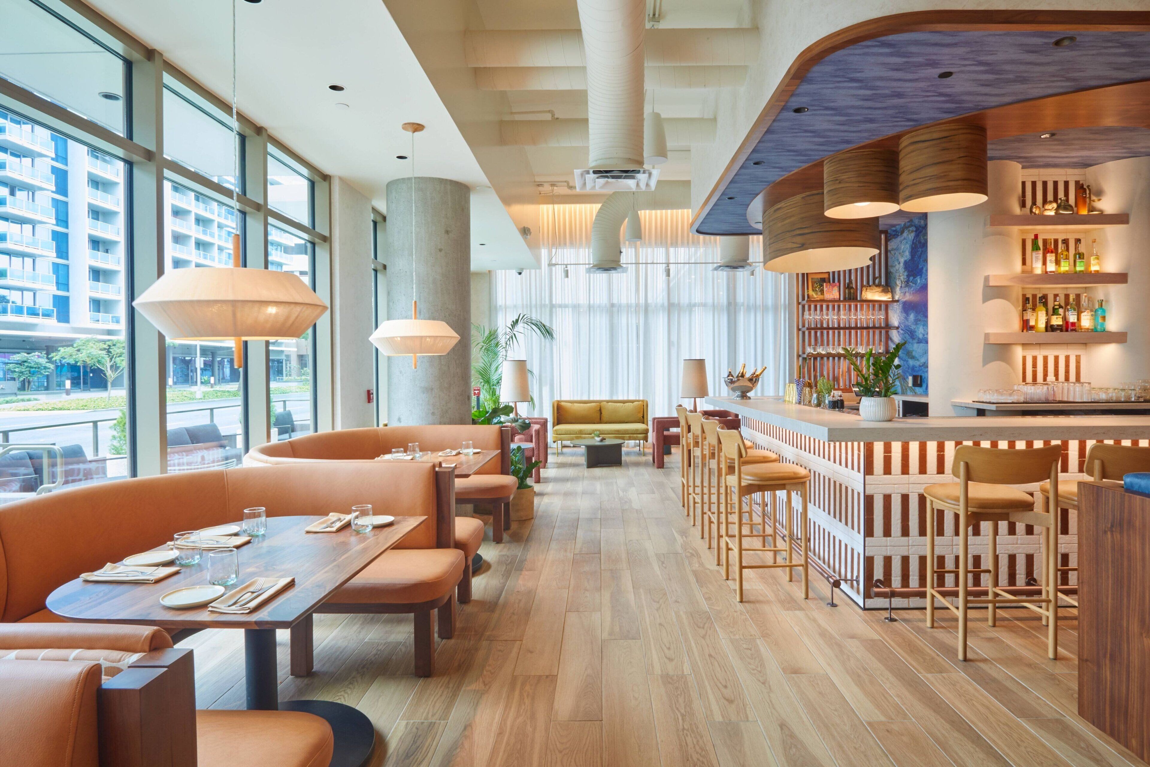 Un ristorante moderno con pavimento in legno, sedute arancioni e un'area bar con scaffali pieni di bottiglie.