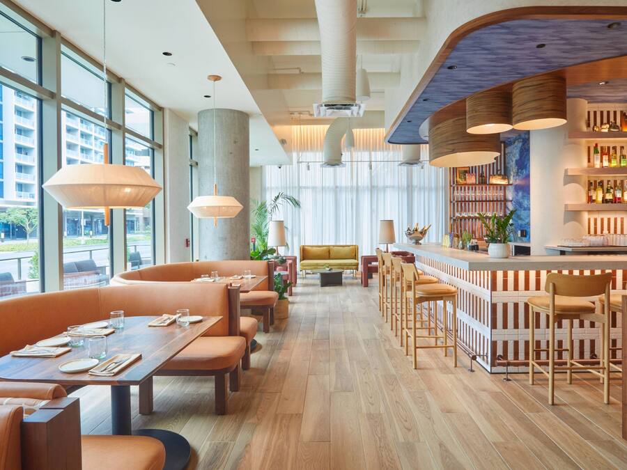 Un ristorante moderno con pavimento in legno, sedute arancioni e un'area bar con scaffali pieni di bottiglie.
