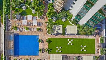 Vista aérea de un complejo turístico con piscina, tumbonas y un jardín ajardinado.